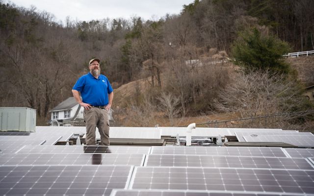 Man standing on a roof surrounded by a solar power installation. 