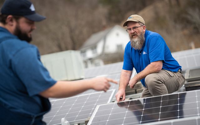Two people look over solar installation on a roof. 