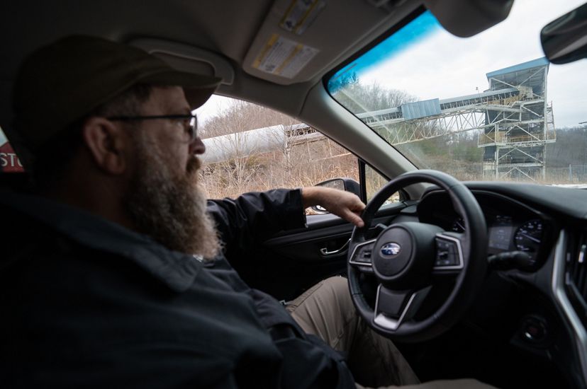 Man driving behind the wheel of a truck as he passes a closed coal mining facility. 