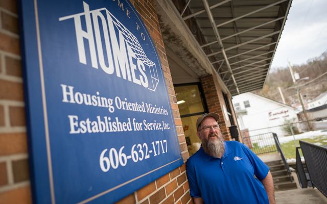 Man in a blue shirt posing next to a sign that reads HOMES, Inc. 