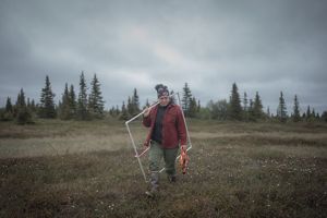 Mary Hostetter carries a PVC quadrat through the tundra on an overcast day. 