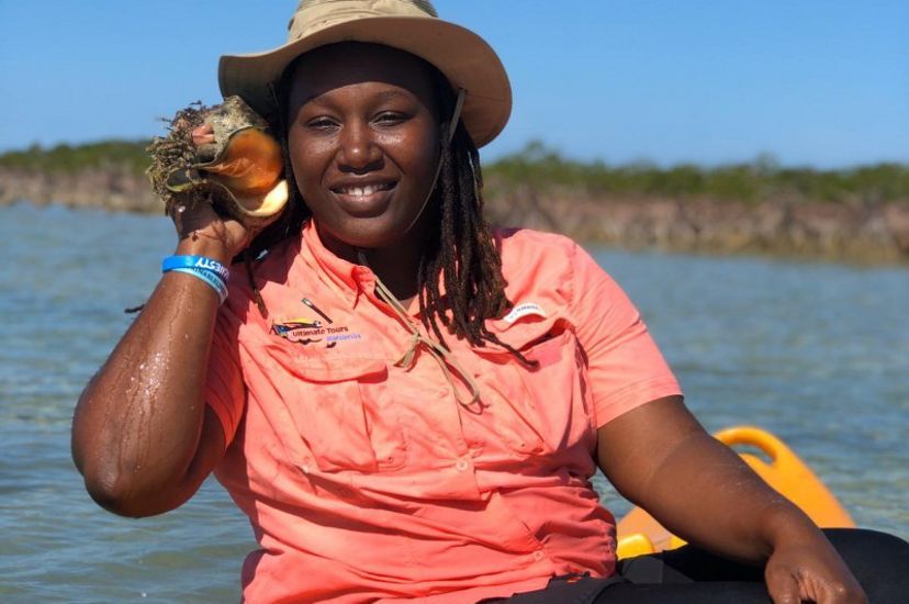 a black woman with a hat holding a queen conch outside