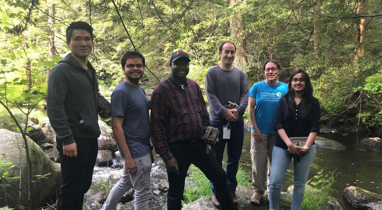 Group of students stand in a forest holding wildlife cameras