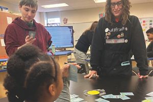 A woman watches as children play a card game.