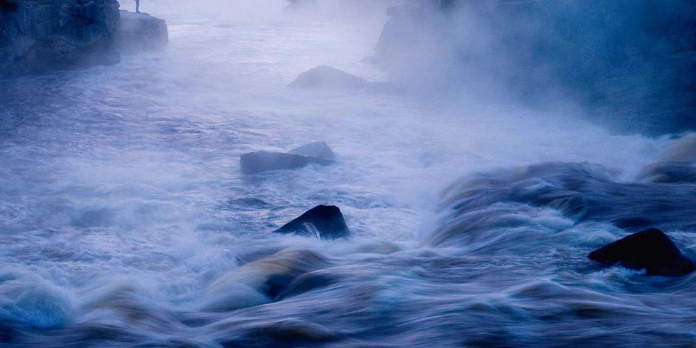 Person fishing at sunrise on a river.