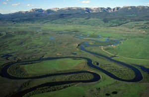 Aerial view of a long river flowing through green pastures.