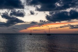 Two small boats float on an ocean under an orange sunset sky.