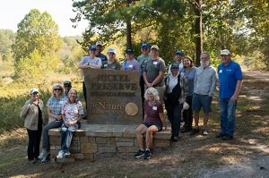 A group of hikers smile next to a sign that reads Nickel Preserve Headquarters.