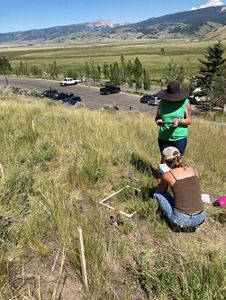 Two people looking down in an outdoor setting with mountains in the background.