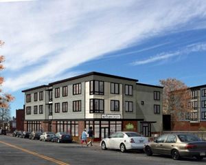 An architectural rendering of a modern, three-story commercial building with dozens of windows and a flat roof under a blue sky.