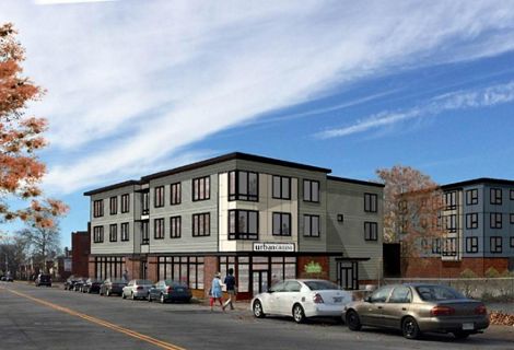 An architectural rendering of a modern, three-story commercial building with dozens of windows and a flat roof under a blue sky.