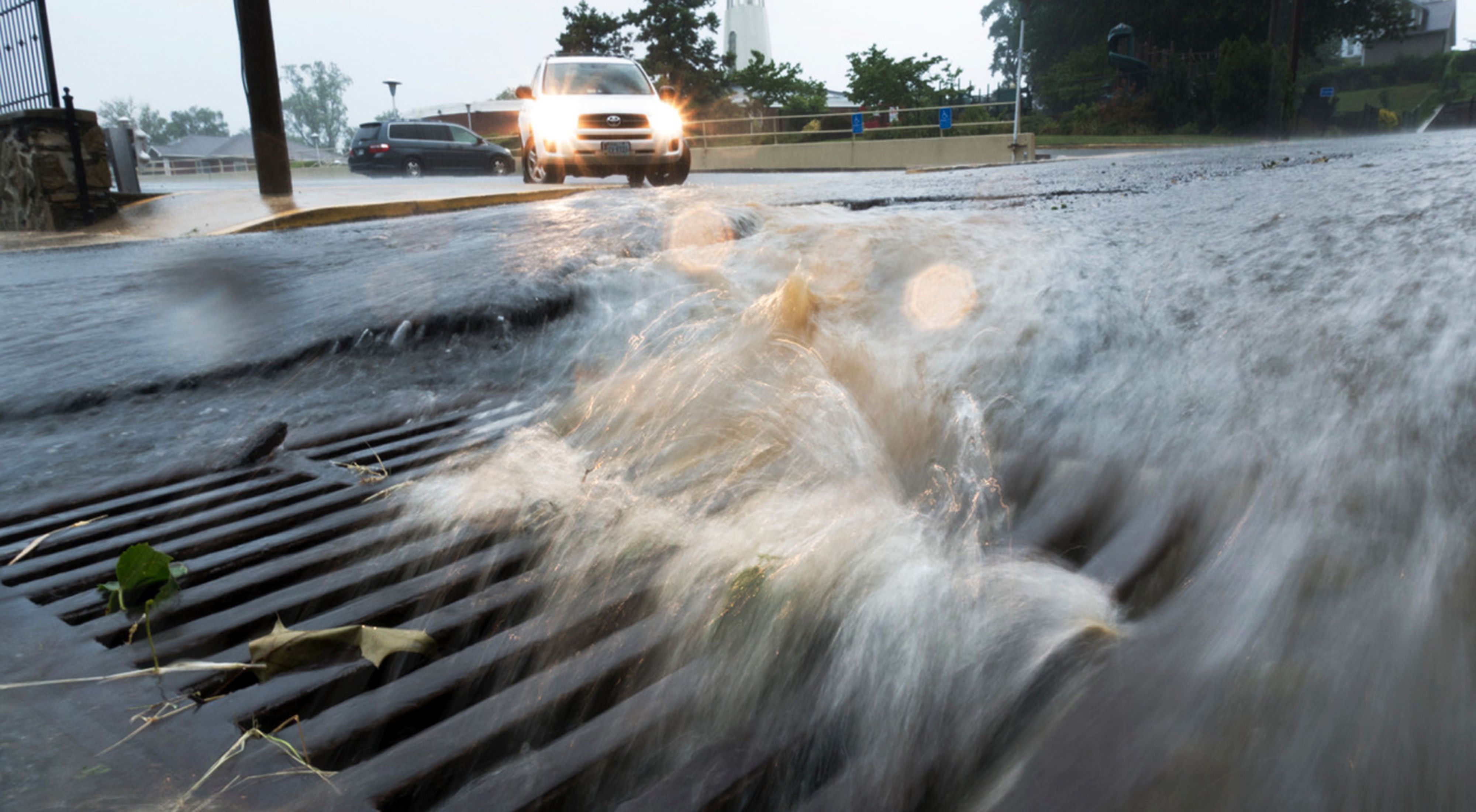 Photo of rushing water running off a street and into a drainage basin.