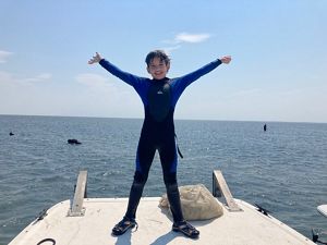 Boy in wet suit raises arms on a dock.