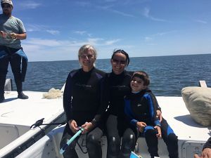 Two women and a young boy hugging and sitting on a boat wearing wetsuits.