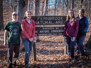 A family of TNC volunteers standing in front of a wooden sign.