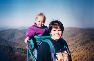 A woman holding a baby in a backpack carrier.