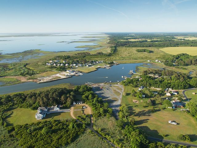 Aerial view of the town of Oyster, Virginia. Houses surrounded by trees and open fields cluster around a wide inlet.  