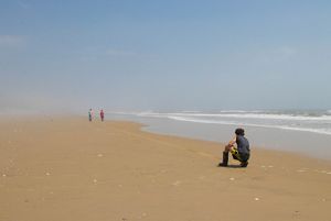 A boy holds the end of a long yellow tap measure stretched out along the beach.