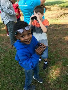 A smiling boy looks up at the camera while holding binoculars.