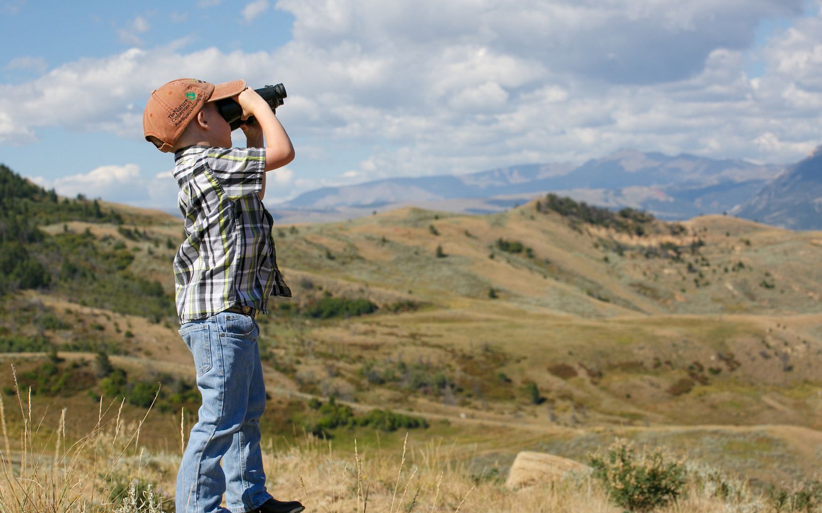 Child with binoculars looking out from a hill. 