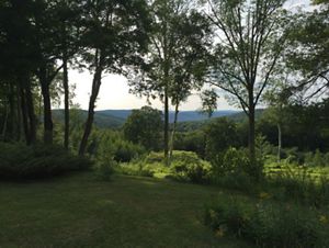 Grassy foreground, surrounded by lush green trees, with green hills in the distance.