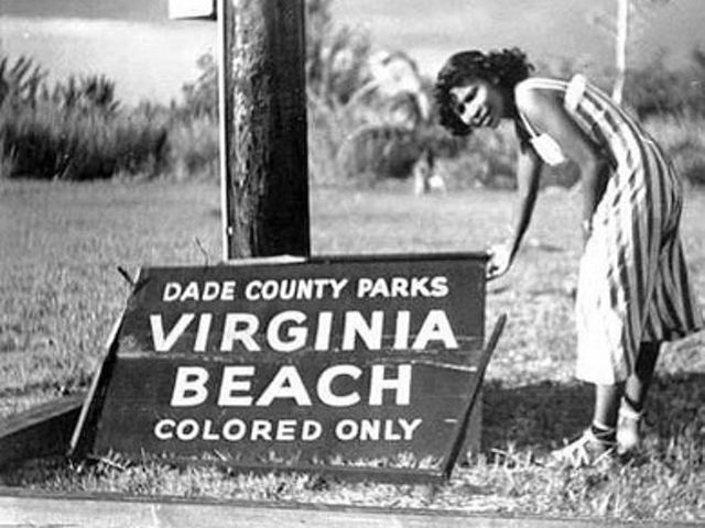 Historical photo of a visitor standing on Virginia Key Beach standing next to a "colored only" sign. 