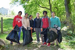Six people pose together during a stream cleanup event. They are holding large black plastic trash bags and carrying long orange grabbers.