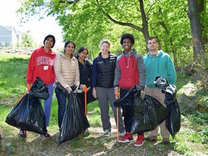 Six people pose together during a stream cleanup event. They are holding large black plastic trash bags and carrying long orange grabbers.
