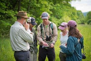 A small group of people gather in a forest and look at a map that one of them is holding.