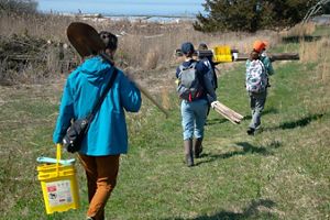Several people holding equipment and tools walk down a grassy path.
