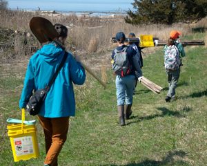 Several people holding equipment and tools walk down a grassy path.