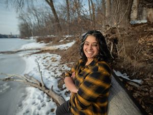 Meera stands on a frozen river bank, wearing a plaid shirt and looks at camera