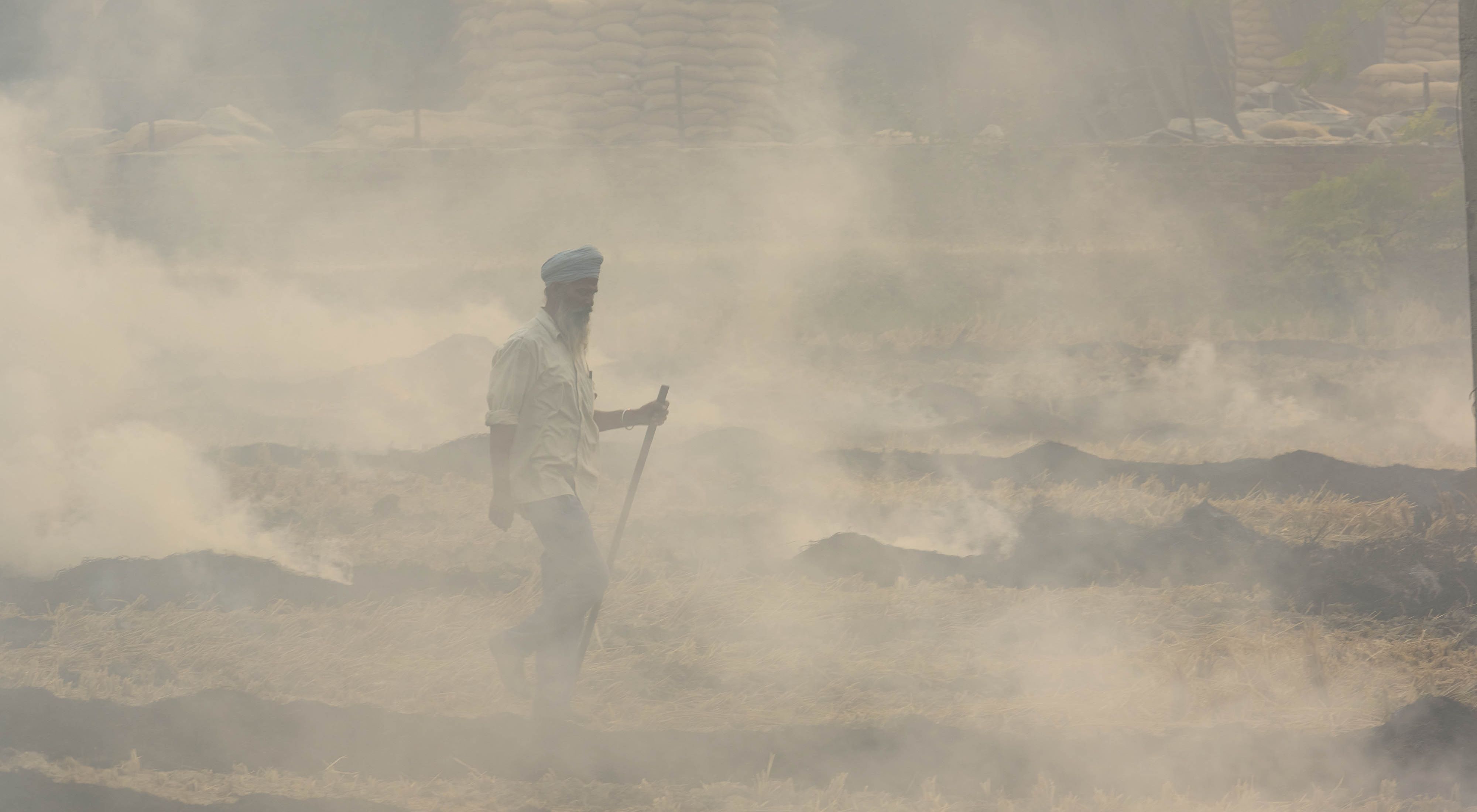 A farmer is obscured by smoke from burning crops on his field.