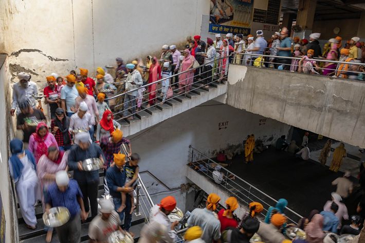 Long lines of people holding empty plates head down a stairwell.