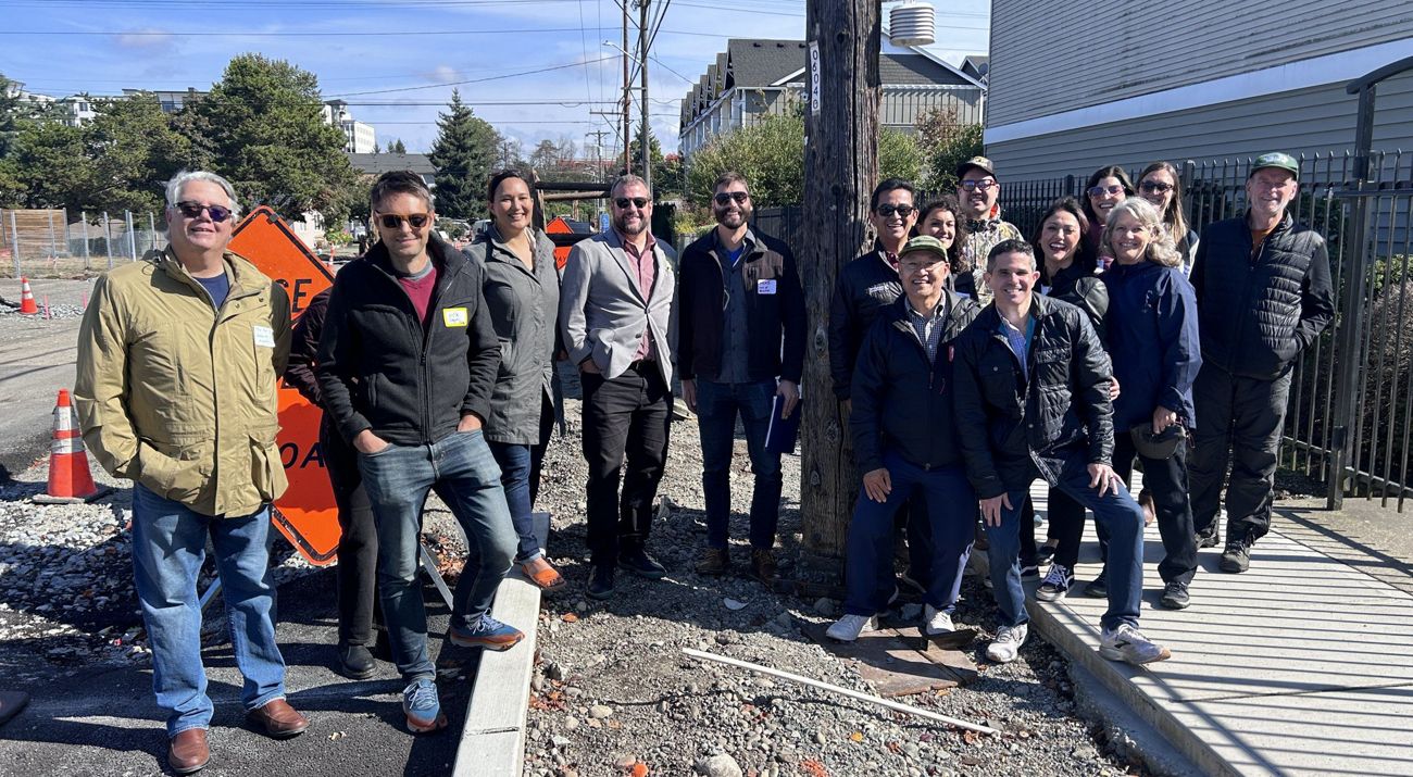 A large group of people stand on an urban sidewalk and smile for the camera.