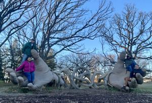 Four people pose on a sculpture of hands in a park for a picture.