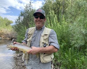 Paul Jewell stands in front of a freshwater stream holding a fish.