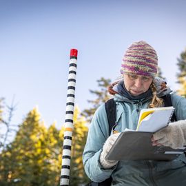 A woman scientist is in a forest and writing down on paper.