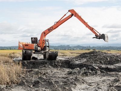 A large orange excavator works to dig a channel in thick mud.