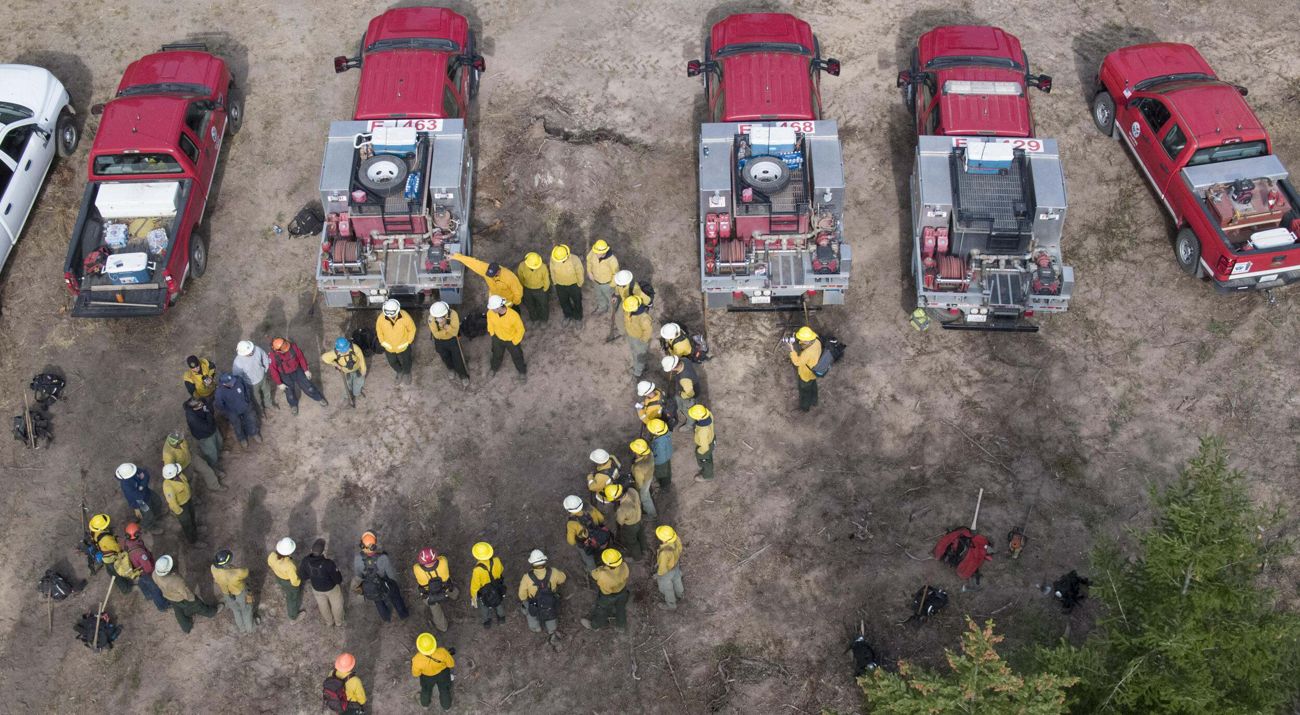 A group of fire practitioners standing around fire trucks.