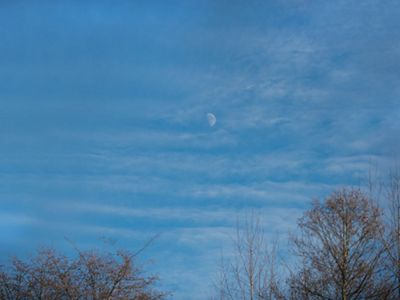 A half moon appears in a blue sky dotted with clouds.