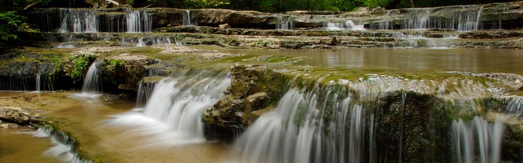 Waterfalls tumble over rocky ledges in a forest.