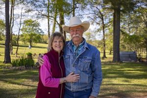 A man and a woman stand together in a field of green grass.