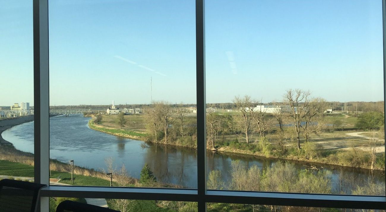 Looking through a window out over a wide river that curves between an industrial area and reclaimed wetlands.