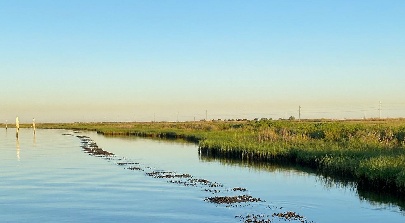 The sun sets over calm waters and an adjacent marsh.
