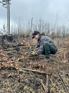 A person wearing a hat kneels down in a field.
