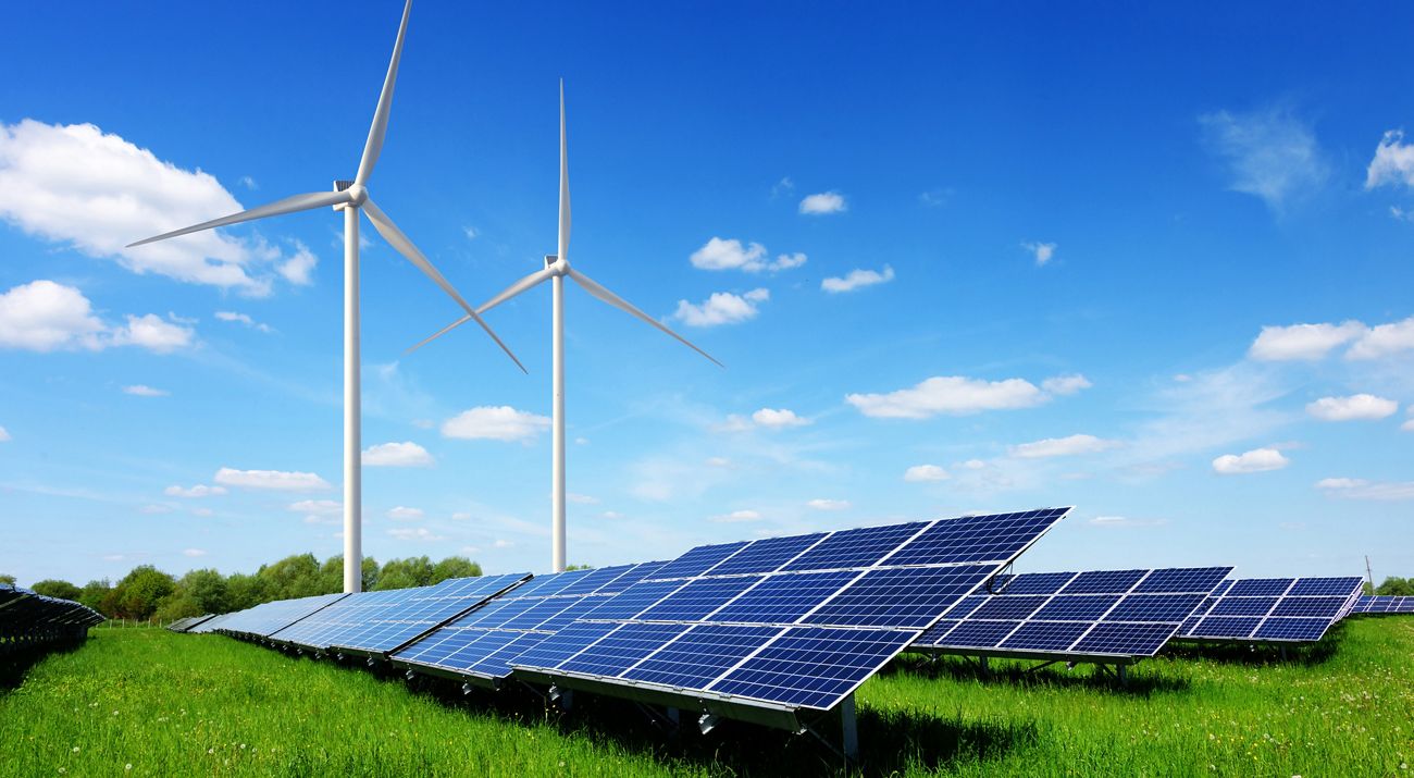 Solar panel and wind turbines on green grass with blue sky background.