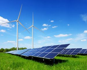Two wind turbines on a solar energy farm against blue sky.