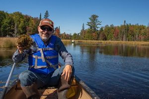A TNC staff member sits in a canoe holding a handful of wild rice seeds, preparing to plant them in a wetland. 