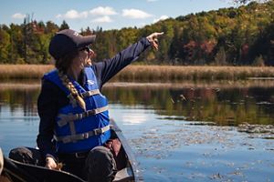 A TNC staff member in a canoe scatters wild rice seeds into the calm wetland waters.